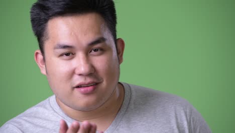 young handsome overweight asian man against green background