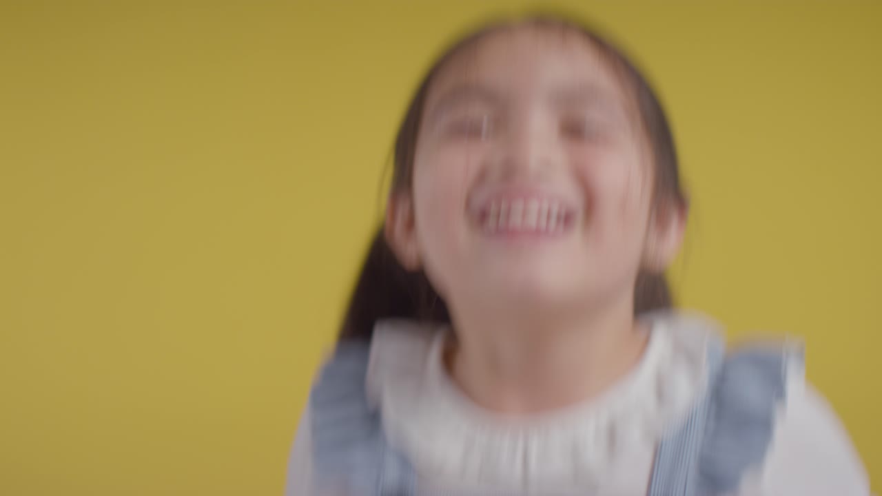 Studio Portrait Of Hyperactive Girl Smiling And Jumping Against Yellow Background