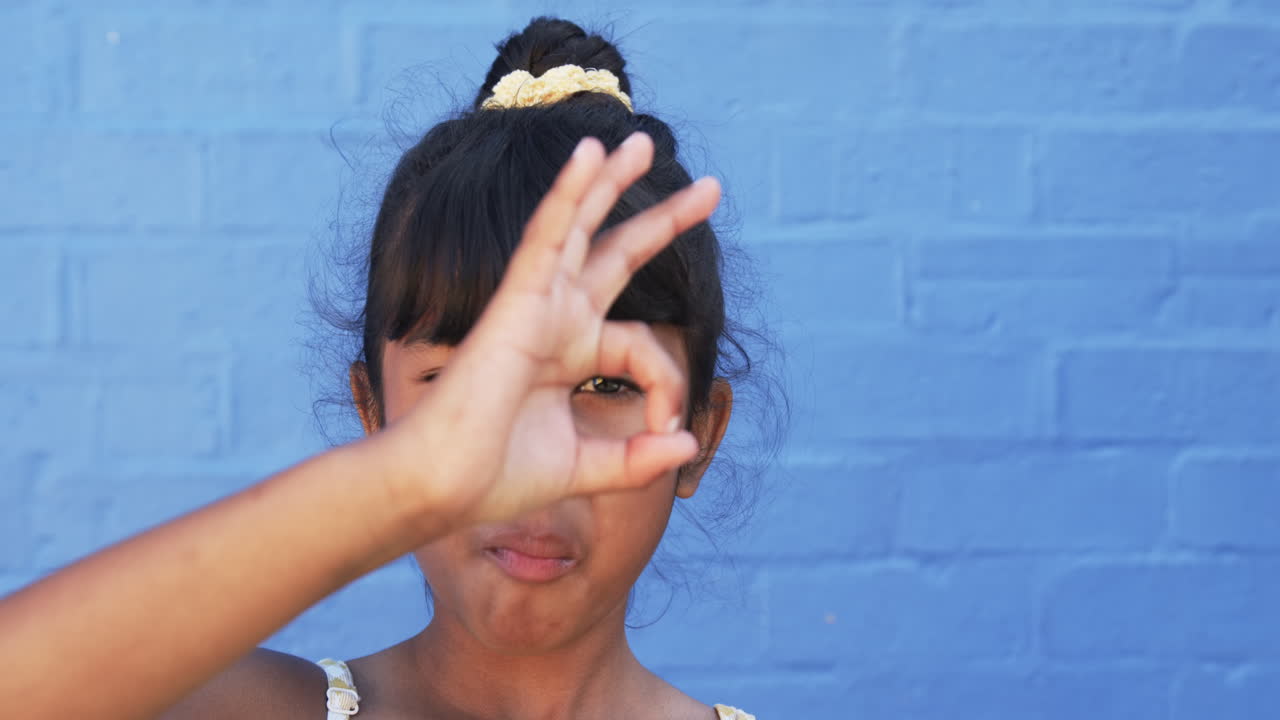 In a school setting, a young biracial girl makes a gesture with her hand