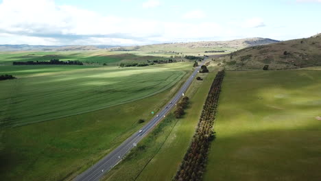 drone pan around highway with cars driving down road surrounded by green fields and trees