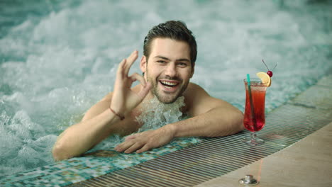 macro de un tipo sonriente haciendo un gesto "ok". un hombre posando para la cámara en una piscina de lujo.