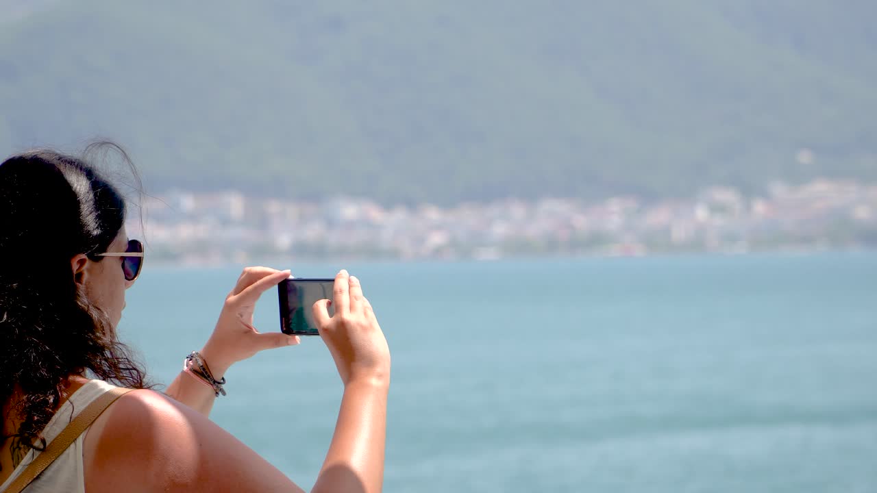 갈색 여성이 스마트폰으로 해양 풍경의 사진을 찍거나 비디오를 만들고, 여름 테마, 실시간 촬영