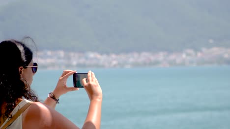 mujer morena toma fotos o hace video de paisajes marinos con un teléfono inteligente, tema de verano, toma en tiempo real