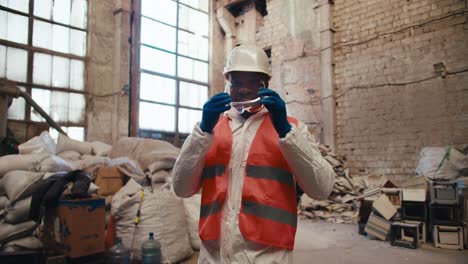 Portrait-of-a-happy-confident-man-with-black-skin-color-in-a-white-uniform-and-orange-worker-at-a-garbage-and-waste-processing-plant.-Male-factory-worker-crosses-his-arms-over-his-chest