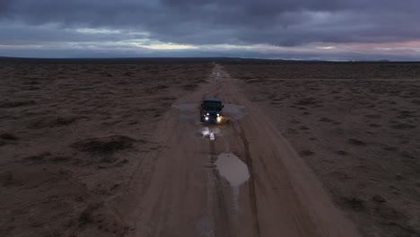 conduciendo un jeep por el desierto de mojave justo después de una fuerte lluvia al atardecer con un cielo colorido - vista aérea