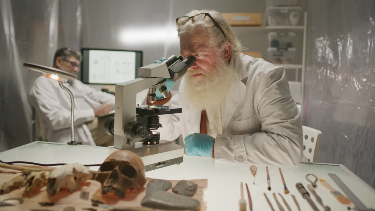 Elderly Archaeologist Examining Sample under Microscope in Laboratory