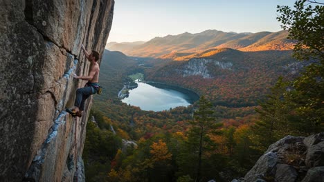 a rock climber ascends a vertical cliff face surrounded by autumn foliage and a serene lake with majestic mountains in the background during golden hour