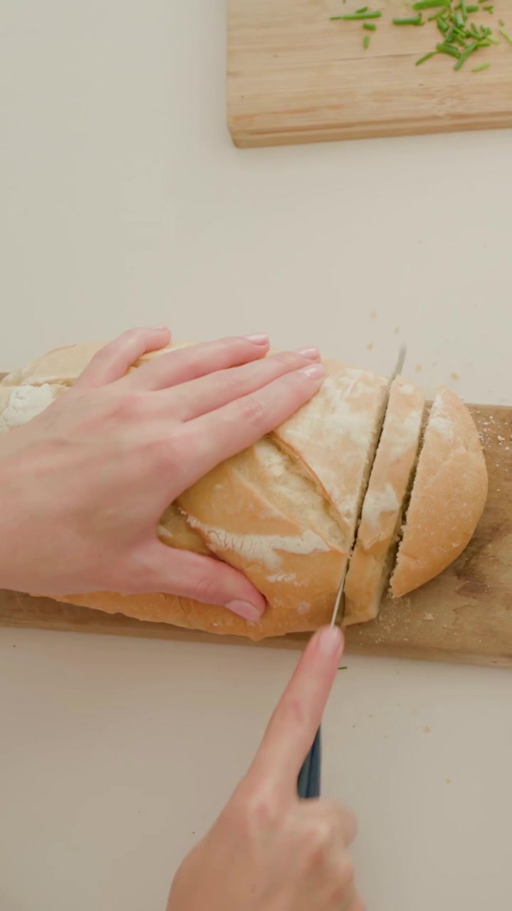 Vertical video: Slicing hands making first cut and sawing loaf with knife on counter, serving