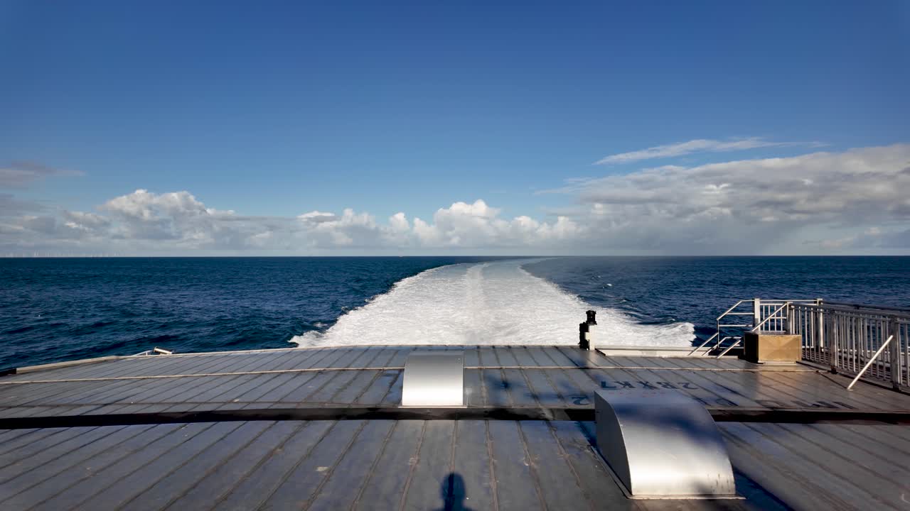 Ship creating white wake travelling over blue Irish Sea under a bright sky