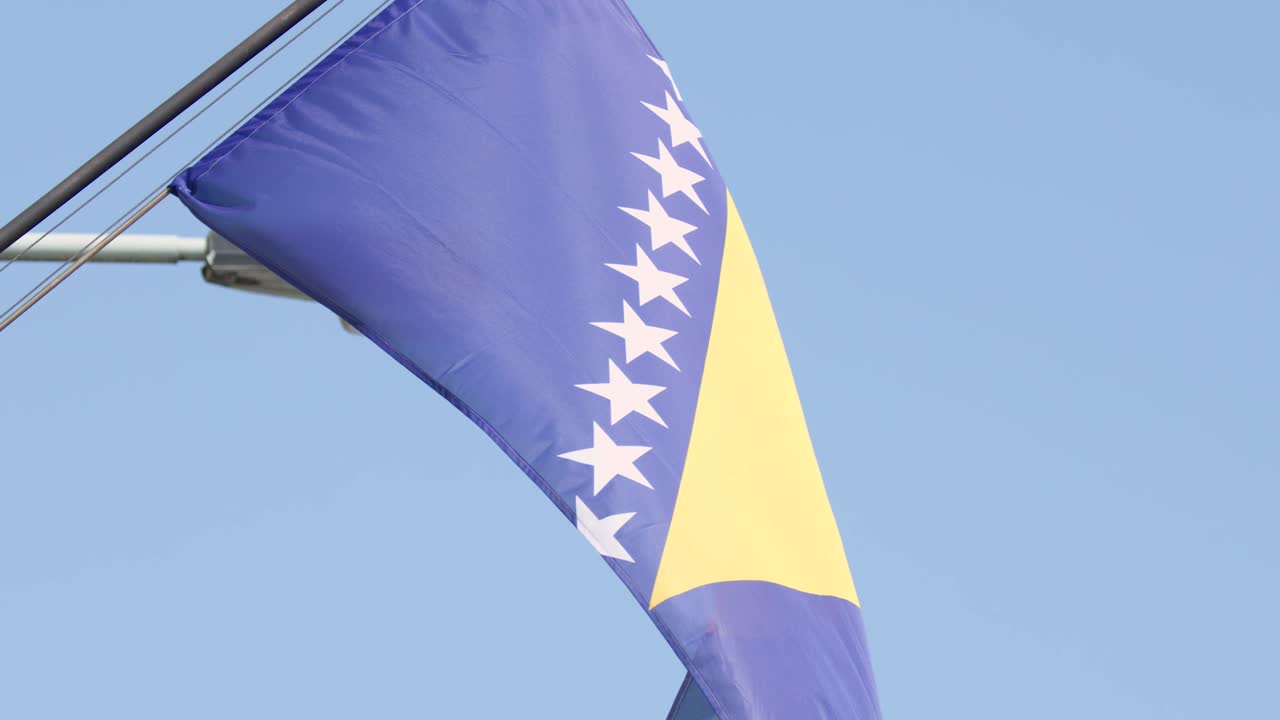Bosnia and Herzegovina flag flutters in daylight, clear sky, city center, steady camera angle