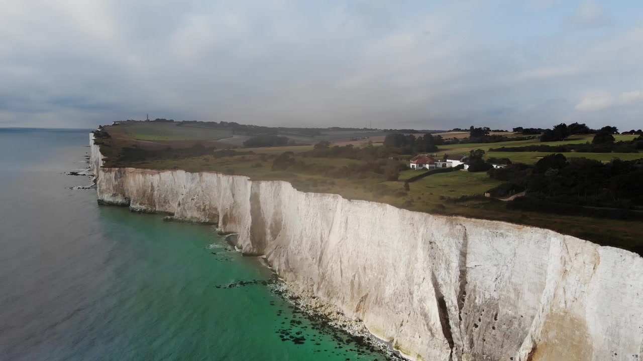 Drone aerial top shot panning left to right over the White Cliffs of Dover, revealing the chalk coastline and turquoise sea in Kent, England, UK. Cinematic 4K video showing the landmark.