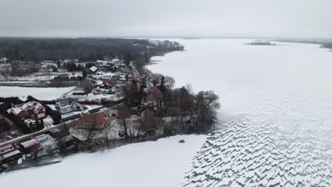 Drone-establishing-overview-of-snow-covered-lake-and-rural-town-near-Suwalki-Gap-Masuria-Poland-in-winter