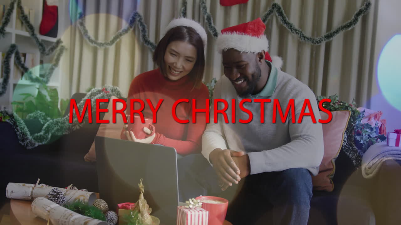 animación de texto de felices navidades sobre una pareja con sombreros festivos usando una computadora portátil