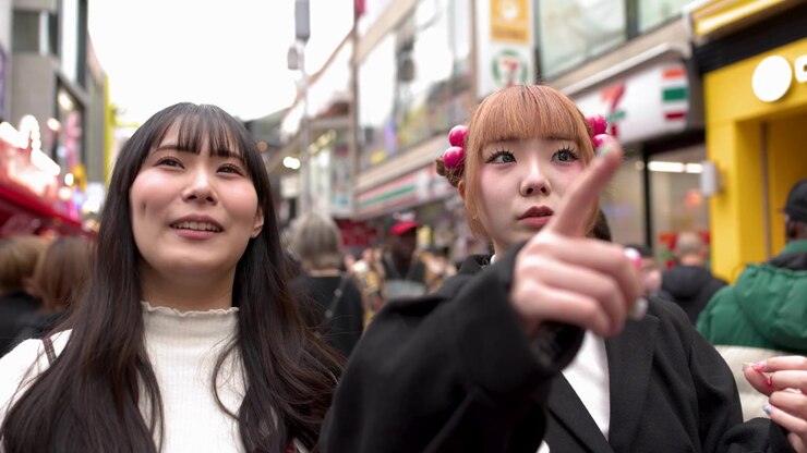 Due eleganti donne asiatiche parlano e indicano mentre camminano tra le strade affollate di Harajuku a Tokyo