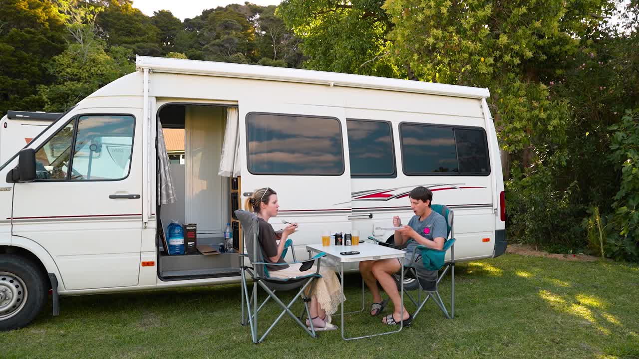Young couple eating dinner in next to the campervan. Time lapse
