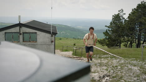 Hiker-with-an-orange-backpack-running-up-the-path-to-the-concrete-monument-on-top-of-mountain-Slavnik-past-the-mountain-cottage