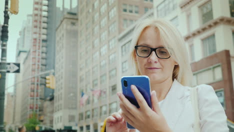 a young woman uses a smartphone against the backdrop of office buildings in downtown manhattan new y