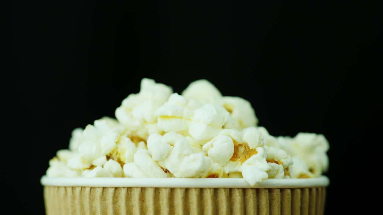 검은색 배경 4k 비디오에서 팝콘 종이 유리가 천천히 부드럽게 회전합니다.