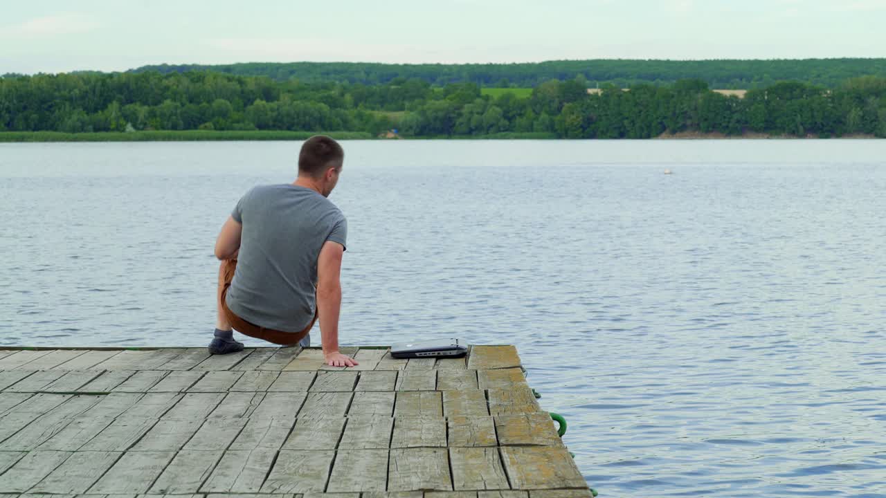 Man with his notebook is working outdoor at the lake. Old wooden pier