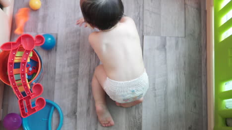 High-angle-shot-of-a-one-year-old-asian-boy-playing-by-himself-with-colorful-toys-inside-an-indoor-playground