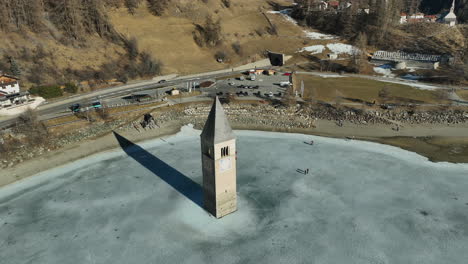 Drone-Toma-Panorámica-Turismo-Caminando-A-La-Iglesia-Hundida-De-Graun-En-Un-Lago-Congelado-En-Italia