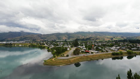 beautiful aerial drone shot over cromwell town along the dunstan lake in new zealand on cloudy day with the view of mountain range in the background