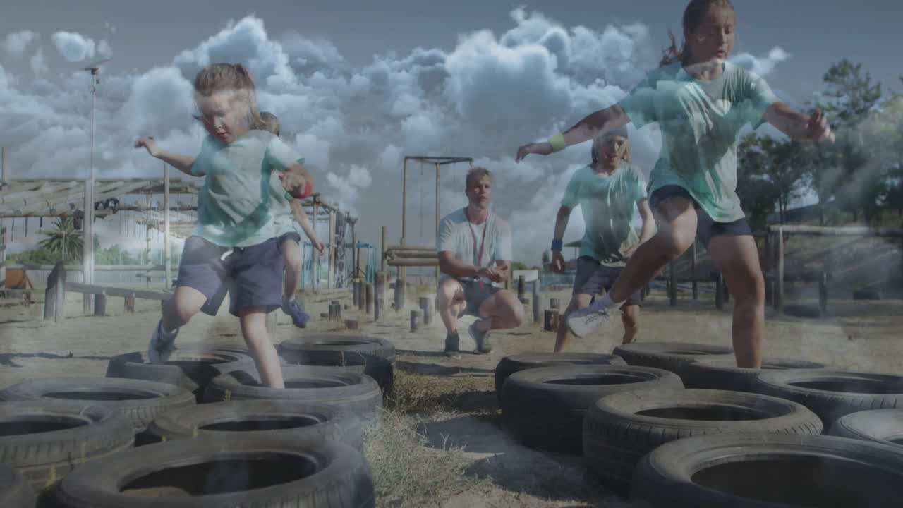 Running through tire obstacle course, children playing under cloudy sky at school