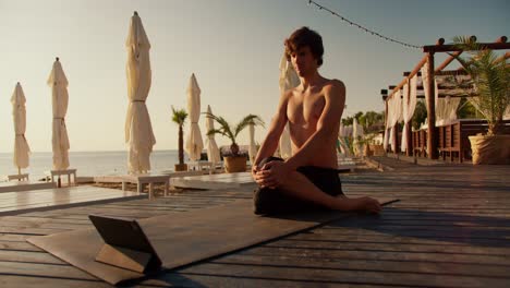 Der-Typ-Macht-Yoga-Und-Schaut-Sich-Ein-Trainingsvideo-Auf-Dem-Tablet-An.-Online-Sport-Am-Sonnenstrand-Am-Morgen