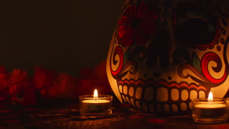 still life of decorated skull mask surrounded by candles and flowers celebrating mexican holiday of dia de muertos or day of the dead against dark background