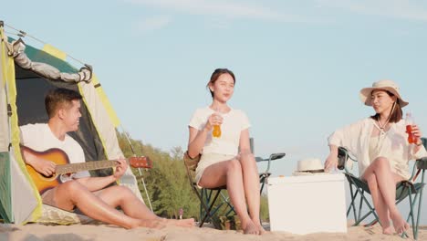 happy friends with drinks in camp and laughing together in holidays on sand beach near camping tent vacation time at sunset