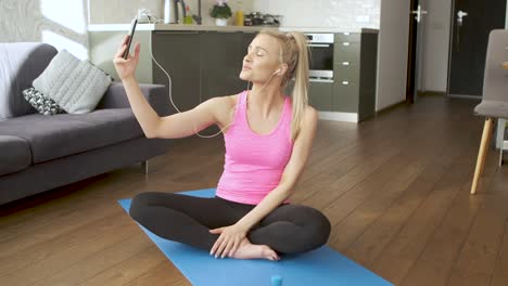 young attractive sporty woman sitting on yoga mat making selfie with her mobile phone