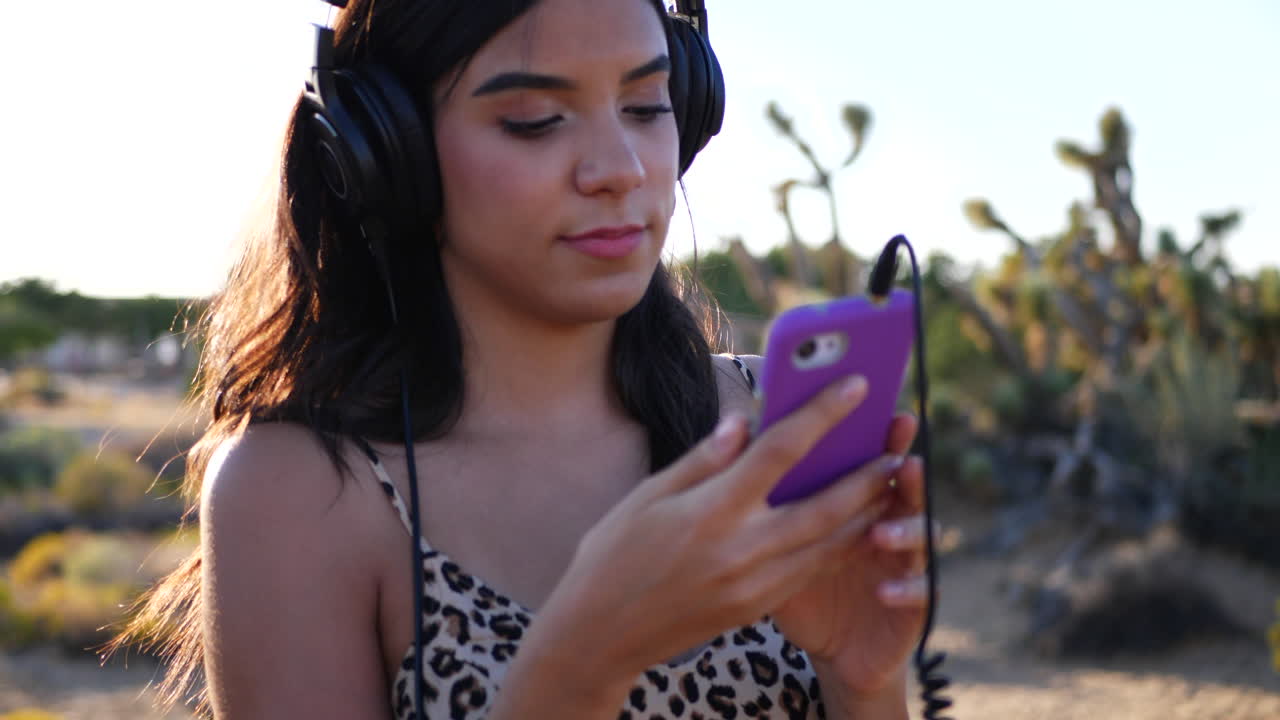 A beautiful young woman picking a song to listen to on her headphones outdoors in nature SLOW MOTION