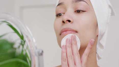 Biracial-woman-with-towel-washing-her-face-in-bathroom