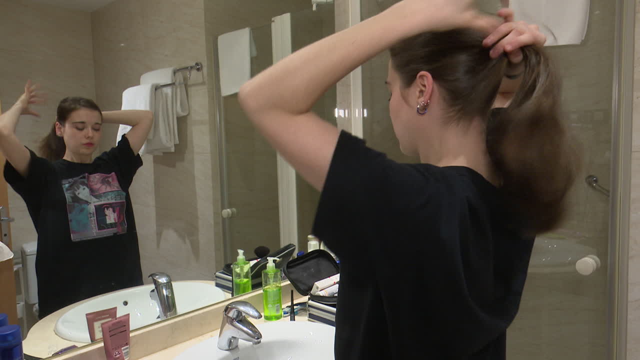 Woman brushing and tying up her hair in the bathroom