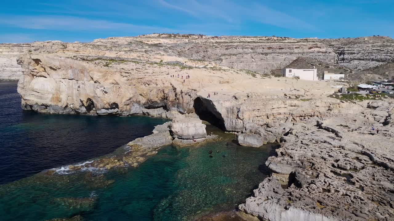Ripresa aerea con drone della Dwejra Hole a Gozo, Malta, che mostra subacquei in acque cristalline, filmato di viaggio cinematografico in 4K 60FPS che mette in evidenza la spettacolare costa calcarea e il paesaggio marino mediterraneo