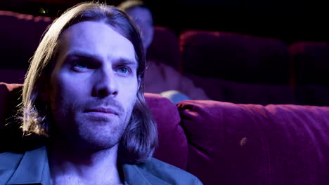 close up view of blond man watching a movie in the cinema with the lights off