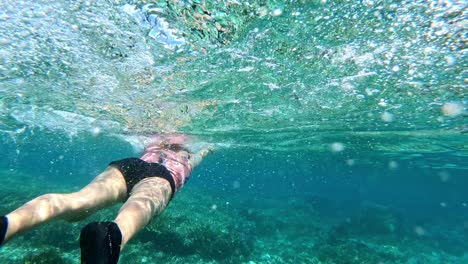 woman swimming along the shallow part of the sea, above the rocky corals