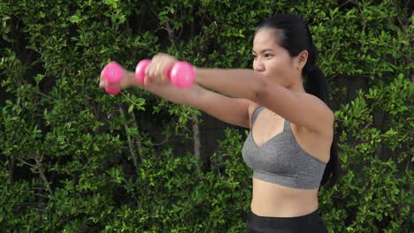 sporty thai woman exercising with dumbbells stretching arms forward and sideways