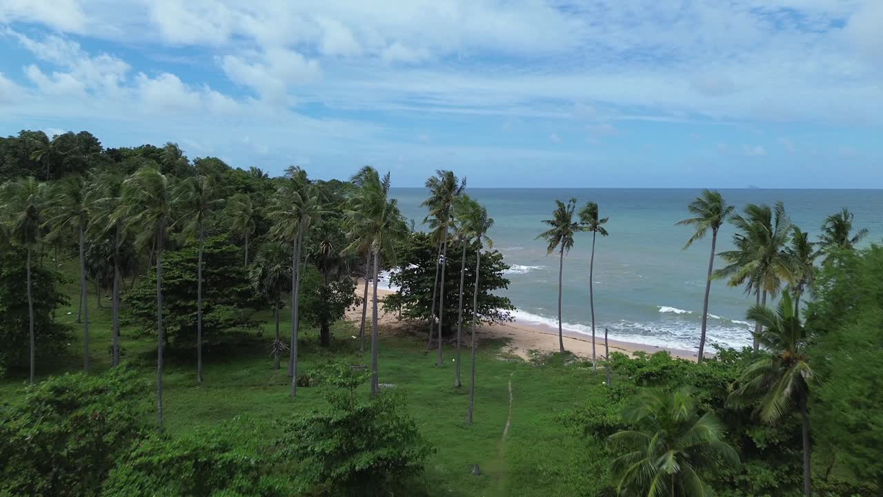 Aerial drone footage of Koh Lanta in Thailand showing longtail boats anchored by the shore, lush palm trees, tropical forest and rocky coastline with scenic turquoise sea