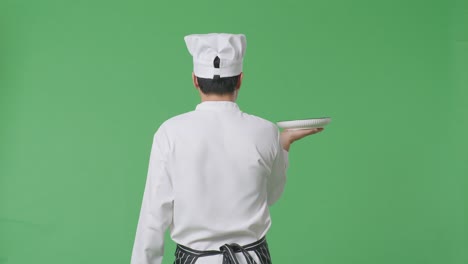 back view of asian man chef holding a dish while walking in the green screen background studio