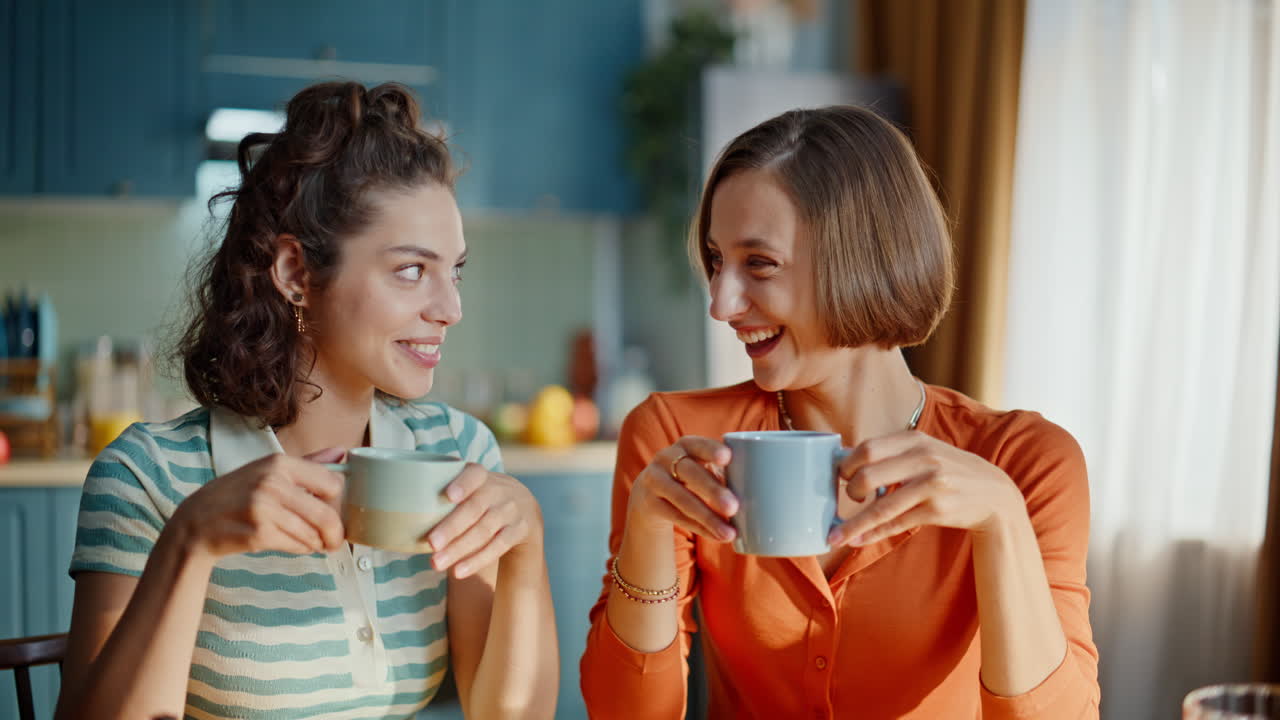 Due sorelle che chiacchierano in cucina tenendo in mano delle tazze di caffè, primo piano. Donne felici.