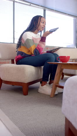 vertical video of african american casual businesswoman talking on smartphone in office lounge