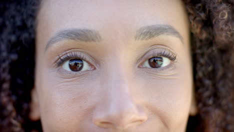 retrato en primer plano de ojos marrones de una feliz mujer biracial con cabello rizado sonriendo al sol, en cámara lenta