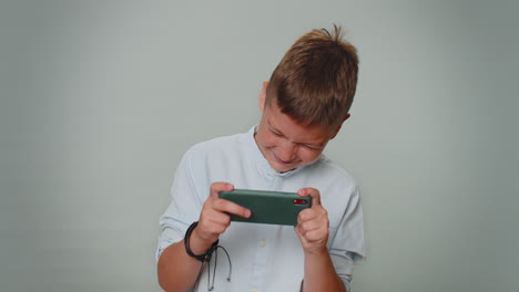 preocupado, gracioso, adicto, niño jugando con entusiasmo a un videojuego de carreras en su teléfono móvil.