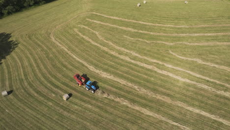 aerial shot of tractor harvesting field with straw harvester, releasing hay bale