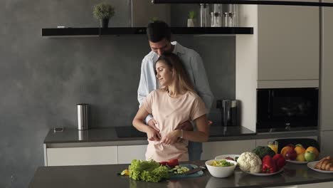 una atractiva pareja joven caucásica se conoce temprano en la mañana en la cocina moderna de la casa. de pie frente al mostrador abrazándose y luego la esposa besando a su marido. feliz pareja casada disfrutando de la mañana