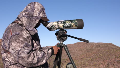 cazador usando un telescopio para buscar animales en camo completo