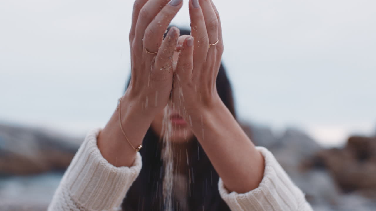 ビーチで指を通って砂を流す女性の手を閉じる