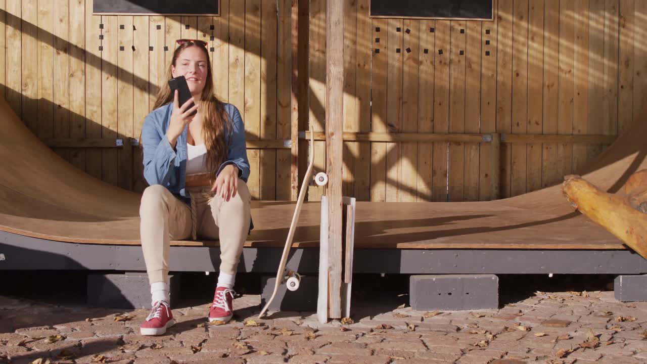 행복한 백인 여성 스케이트보더가 휴식을 취하고 스마트폰을 사용하는 비디오