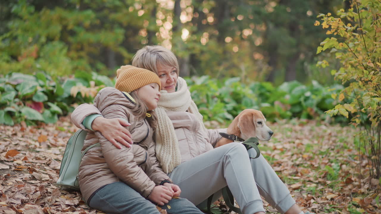 mom gently places arm around daughter while sitting beside dog on autumn leaves in peaceful forest setting, comforting and embracing her in calm moment surrounded by golden foliage